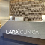 Mostrador de recepción moderno y luminoso con el logotipo de Clínica Lara, destacando un diseño elegante con paredes texturizadas y luz cálida.